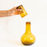 Amber handblown glass vase being held by a hand on a white background