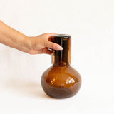 Hand holding a chocolate brown glass bottle carafe against a white background
