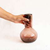 Hand holding a glass cup that serves as a lid to amethyst glass carafe