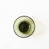 A top-down view of a translucent olive green handblown glass bowl with a dark rim, set against a plain white background.