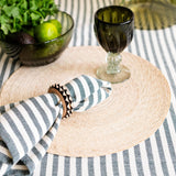 Table setting with an olive green glass, olive green striped cloth napkin and decorative elements on a striped tablecloth.