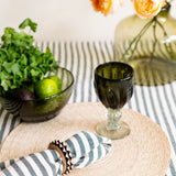 Table setting with an olive green glass, striped cotton napkin, and decorative elements on a hunter green striped tablecloth.