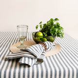 Table setting with striped hunter green tablecloth, clear wine glass, cloth napkin, and glass bowl of greens.
