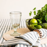 Clear wine glass on a striped hunter green cotton tablecloth with a bowl of limes and cilantro