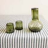 Green glass carafe and two olive green tumblers on a hunter green striped cotton tablecloth