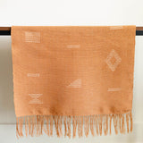 Terracotta cotton table runner with geometric designs hanging on a table and white background