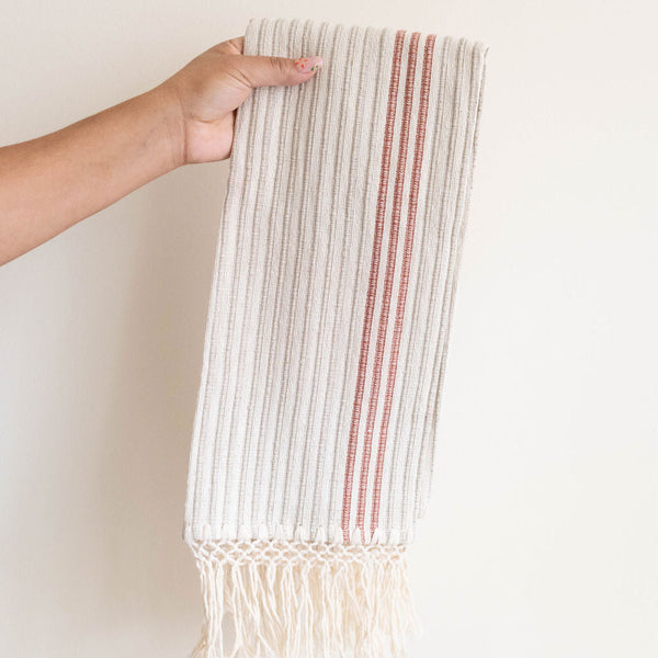 A Corded Handwoven Cotton Hand & Tea Towel with three cinnamon stripes hanging from a hand.