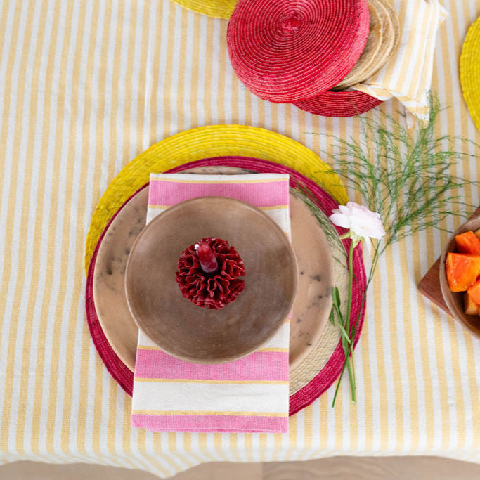 Border Accent sustainable Palm Round Placemat in pink styled on a yellow stripe table cloth