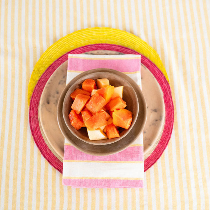 Border Accent sustainable Palm Round Placemat in pink styled with a cotton pink, yellow stripe napkin and yellow placemat.