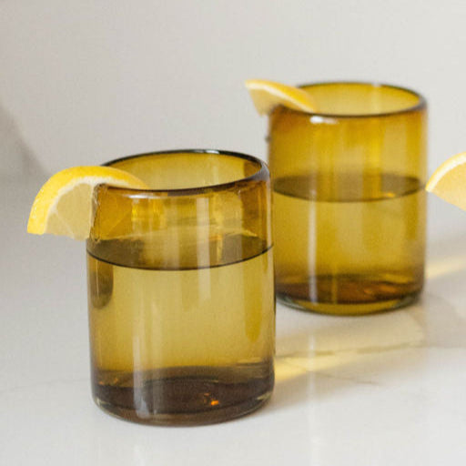 Two Mexican handblown recycled amber glass tumblers with lemon wedges on a light background