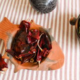 Two ceramic bowls with dried red chilies and green fruits on a striped fabric background