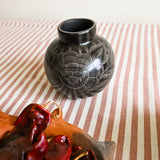 Black decorative vase on a striped fabric surface with red chili peppers.