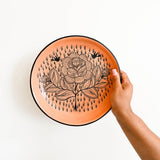 Hand holding a Peach Ceramic plate with a floral design on a white background