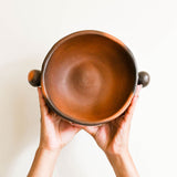 Person holding a brown ceramic bowl against a light background