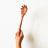 Wooden spaghetti spoon with a unique design held by a hand