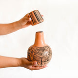 Peach Ceramic vase with floral patterns being held by a hand against a white background