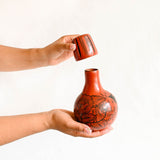 Person holding a red ceramic vase with black floral patterns on a white background
