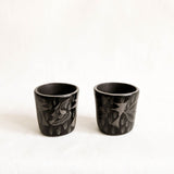 Two black ceramic cups with floral patterns on a white background