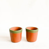 Two terracotta cups with green textured rims on a white background