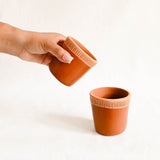 hand holding a terracotta ceramic cup with ribbed textured lines on a white background