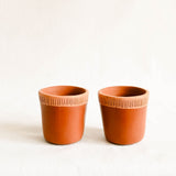 Terracotta ceramic cups with ribbed textured lines on a white background