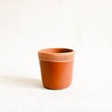 Terracotta ceramic cup with ribbed textured lines on a white background