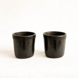 Two black ceramic cups with textured rims on a white background