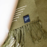 Olive green woven hand towel with fringes and a visible brand label on a neutral background