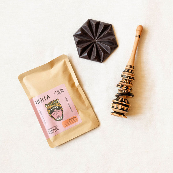 Hijita Mexican Cacao packaging with a chocolate bar and wooden muddler molinillo on a white background