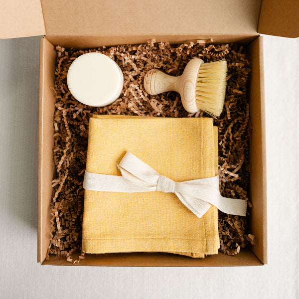 A gift box with plastic-free dish bar soap, an agave fiber brush and a set of cotton woven dinner napkins