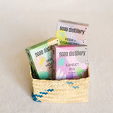 Handcrafted Soap Distillery Trio Soap Bar Gift Basket featuring three artisan soap bars: Beer + Cigarettes, Mint Mojito, and Sunset Fig, each nestled in a small palm basket. Each soap bar is uniquely scented and handmade, with rich, earthy and refreshing notes that evoke craft cocktails and natural essences, wrapped together for an aromatic and artisanal gift experience.