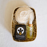 A beautifully curated gift set featuring a Nopalera Noche Clara Soap Bar, an exfoliating Agave Body Sponge, and Sanara Skincare's Chilean Rosehip Seed Body Oil, all elegantly arranged in a handcrafted palm gift basket. This collection is perfect for a luxurious self-care ritual, blending artisanal Mexican products with nourishing ingredients.