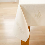 Corner view of Teia Handwoven Cotton Tablecloth on a Table. Tablecloth in a beige neutral color featuring intricate geometric designs, crafted by artisans in Oaxaca. Perfect for adding a touch of elegance and tradition to your dining space. Sustainable and made from 100% Mexican cotton. Ideal for modern and rustic decor styles.