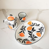 Enamel Peltre serving tray, kettle, and cup in white with delicate orange floral accents inspired by the cempasúchil flower. 