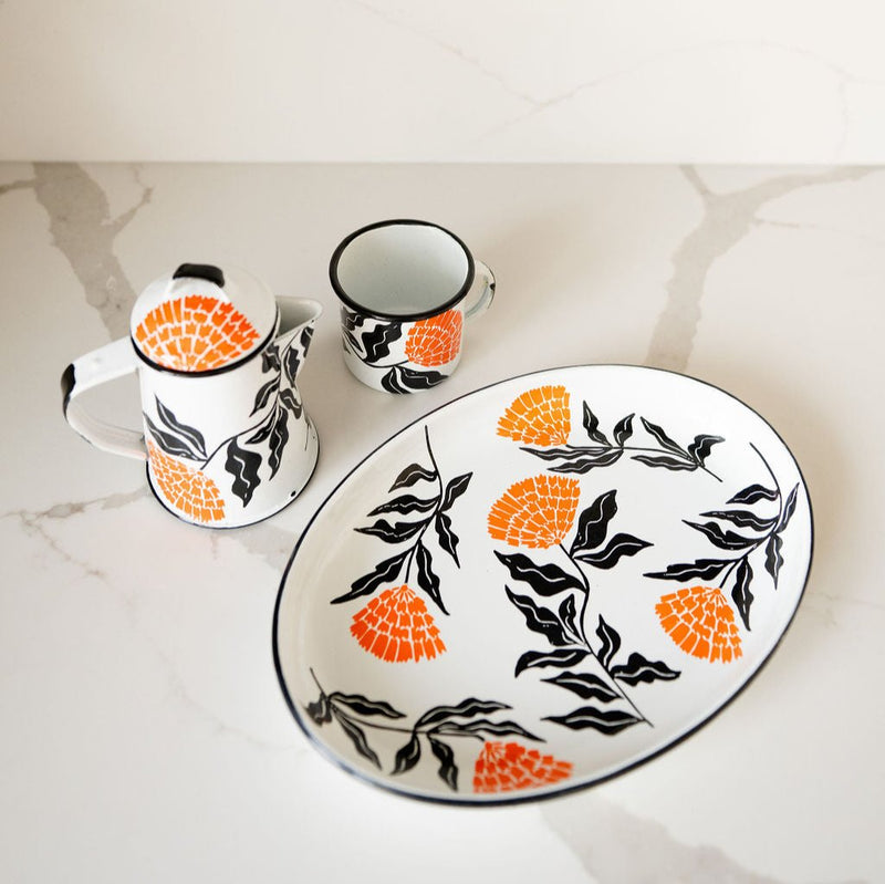 Enamel Peltre serving tray, kettle, and cup in white with delicate orange floral accents inspired by the cempasúchil flower. 