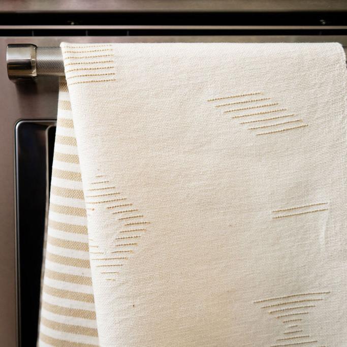 Closeup of gold / beige geometric lines on a handwoven Cotton Tea Towel and Hand Towel hanging from a stove