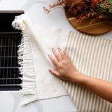 Hand wiping down marble counter using a handwoven Cotton Tea Towel and Hand Towel in Beige Stripes and Geometric Lines with Fringe