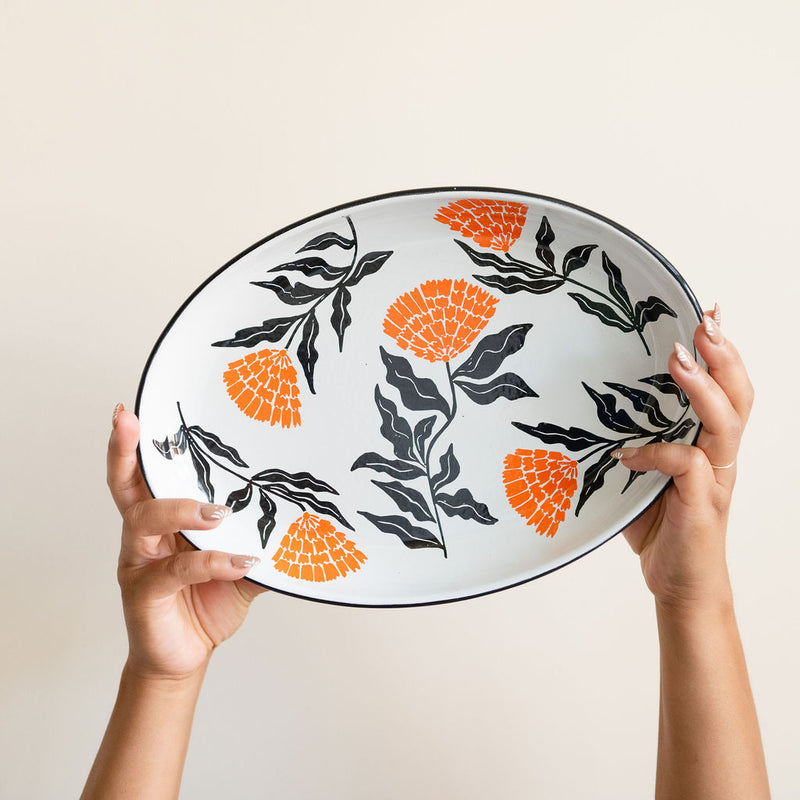 Enamel Peltre serving tray in white with delicate orange floral accents inspired by the cempasúchil flower. The tray features a smooth, glossy finish and raised edges for easy carrying, perfect for serving snacks, or as a decorative centerpiece.