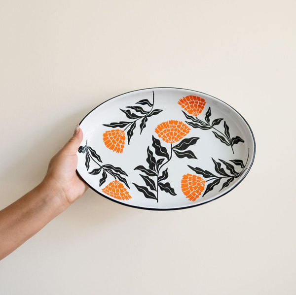 Enamel Peltre serving tray in white with delicate orange floral accents inspired by the cempasúchil flower. The tray features a smooth, glossy finish and raised edges for easy carrying, perfect for serving snacks, or as a decorative centerpiece.