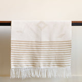 Handwoven cotton table runner in soft, neutral tones with subtle geometric patterns and fringed edges, styled against a light background