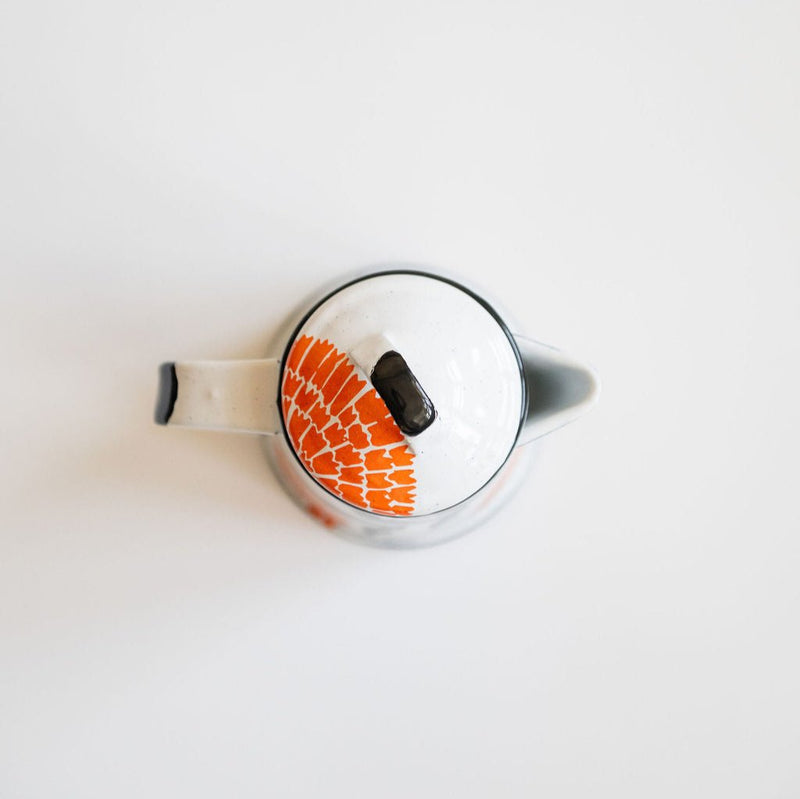 Top view of a white enamel (peltre) kettle with vibrant orange marigold designs and black leaf accents, set against a white background.