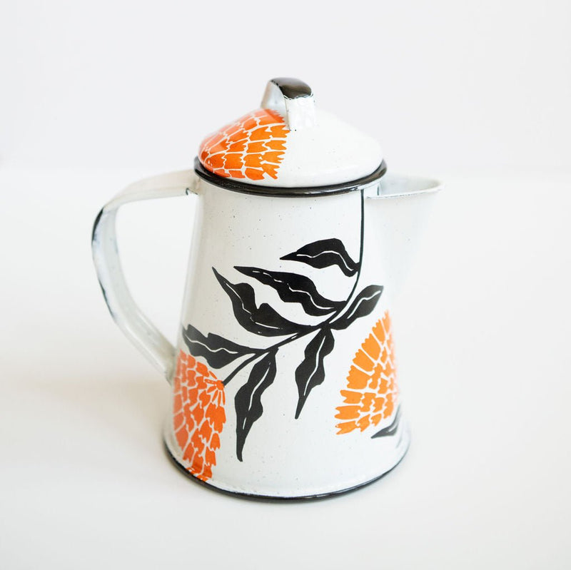 White enamel (peltre) kettle with vibrant orange marigold designs and black leaf accents, set against a white background.