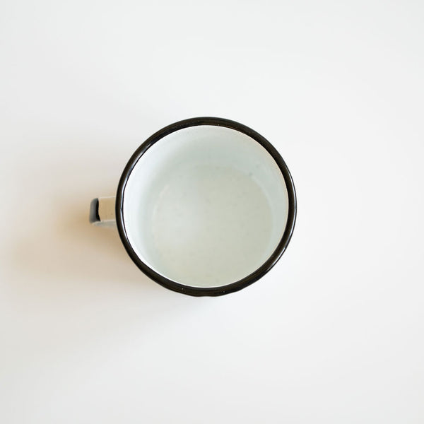 Top view inside a white enamel (Peltre) Cup with vibrant orange marigold (cempasúchil) designs and black leaf accents, set against a white background.