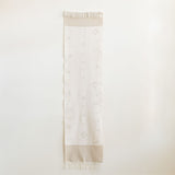 Handwoven cotton table runner in soft, neutral tones with subtle geometric patterns and fringed edges, styled against a light background