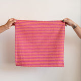 Rosa Mexicano Pink and Orange Striped Napkin held up by two hands