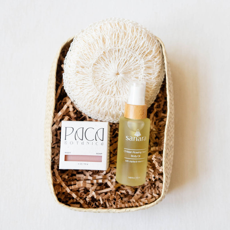 Skincare products including an agave body sponge, a bottle of  Sanara Skincare body oil and Paca Botanica body soap bar with a neutral background