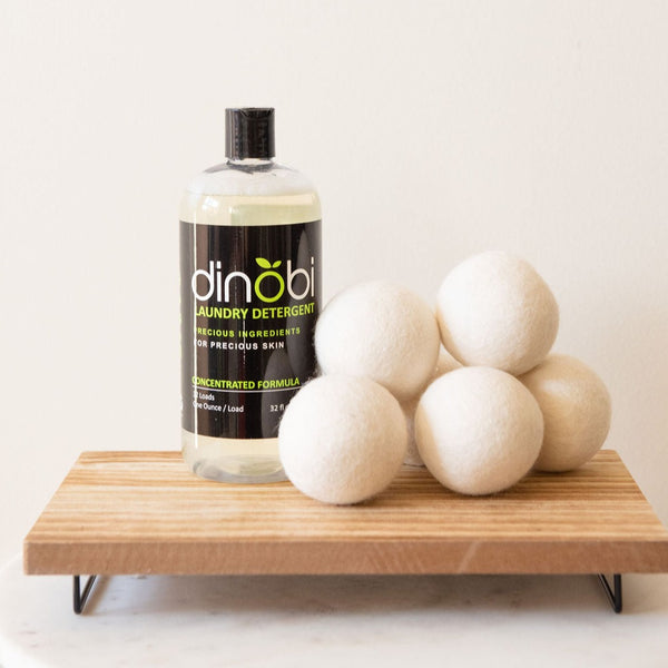 Nontoxic Laundry Starter Set featuring Dinobi Nontoxic Laundry Detergent and 6 wool dryer balls on a wood rack