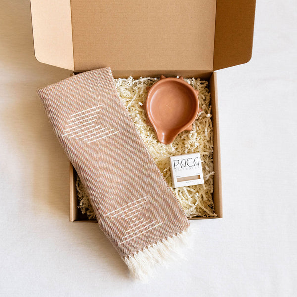 Gift box with a handwoven dish towel, small ceramic soap dish, and soap bar on a white background