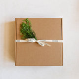 Brown gift box with a sprig of greenery and a white ribbon on a light background