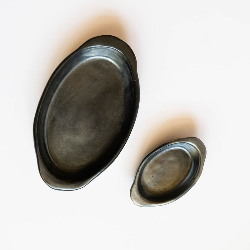 Two oval-shaped ceramic black clay (barro negro) serving dishes on a white background